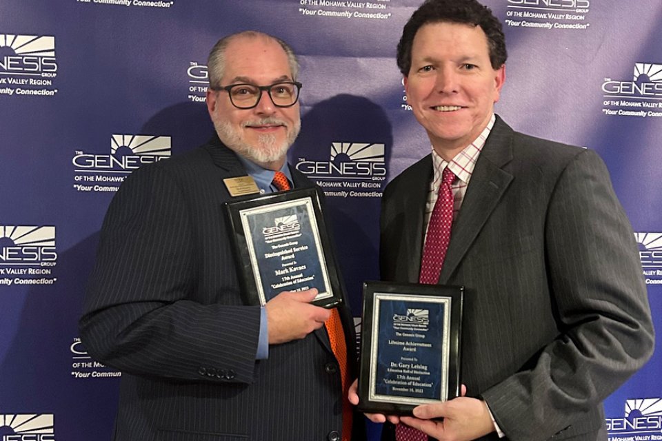 Mark Kovacs and Gary Leising hold up plaques at the Genesis Group's Celebration of Education event in November 2023.